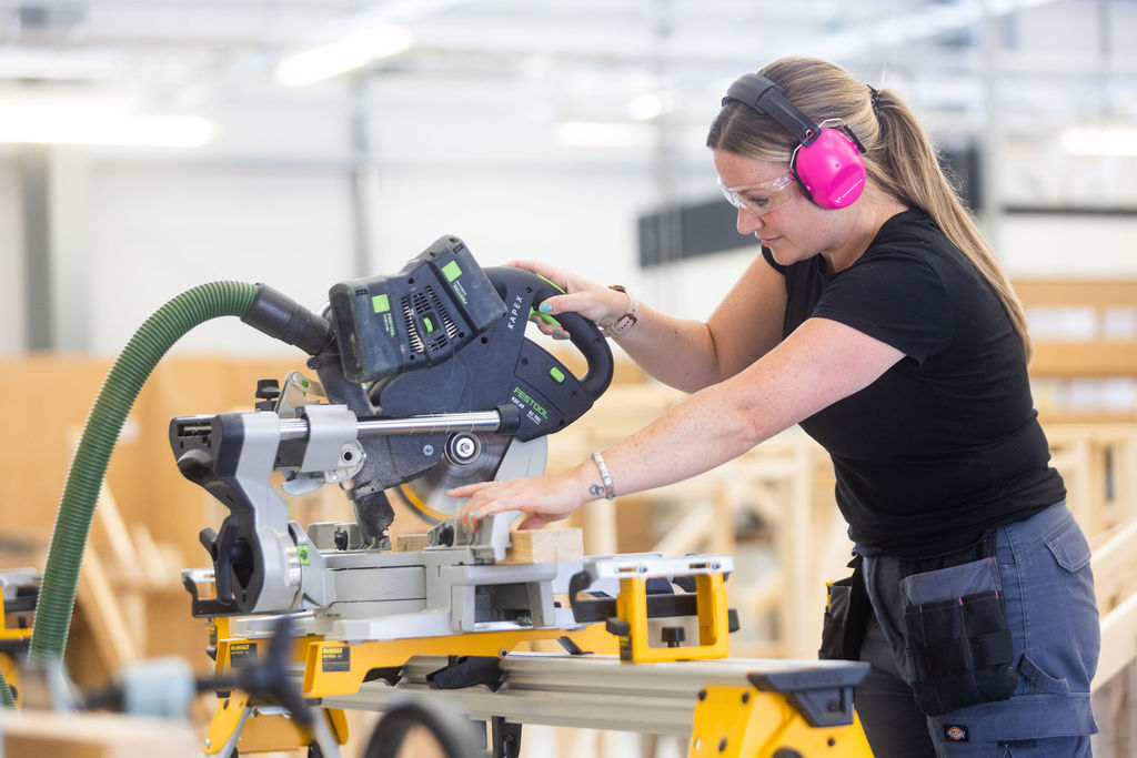Female student using a buzzsaw, wearing ear protectors.