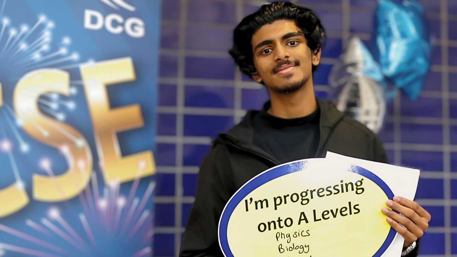 Smiling young man holding a sign with writing on it.